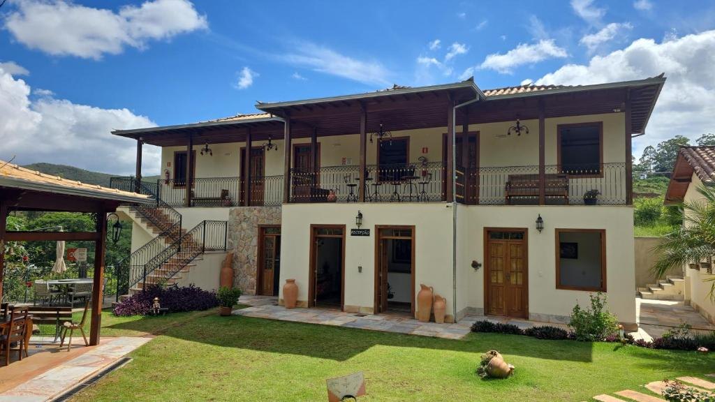 Casarão da pousada, com varanda de madeira e gramado, entre as montanhas